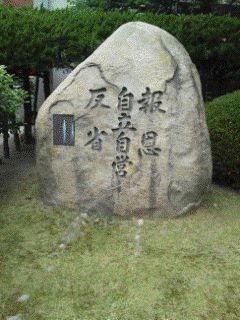 玄関前の芝山にある校訓を刻んだ石碑の写真